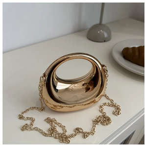 Detail of a gold crescent-shaped mirror finish mini handbag with a fine chain strap