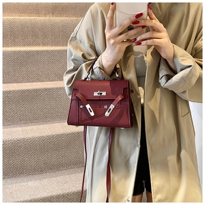 Detail of burgundy lychee-textured leather trapezoid handbag with silver twist lock buckle