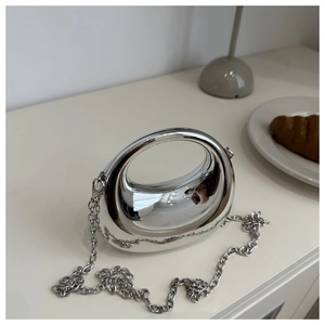 Close-up of silver mirror-finish mini bag with hollow handle and chain strap on white desk