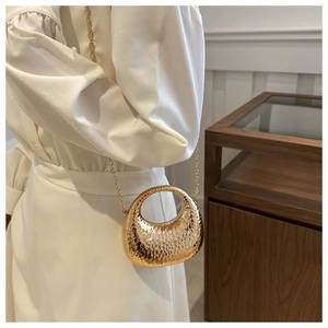 Close-up of a semi-circular golden crescent mini bag with hammered texture and chain