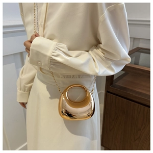 Macro detail of golden mirror pebble bag with circular handle and metal chain strap
