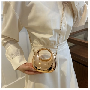 Close-up of a golden mini handbag with metallic mirror finish and chain strap on a model