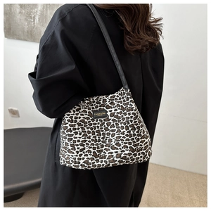 Dettaglio della borsa tote leopardata con tracolla in pelle nera indossata su un cappotto nero