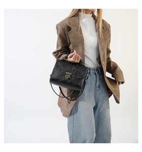 Detail of vintage embossed black handbag with floral patterns and brass metal lock