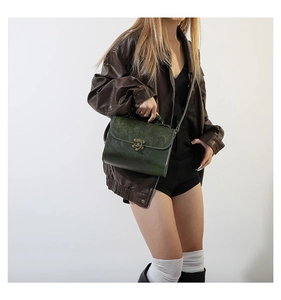 Close-up of vintage dark green leather crossbody bag with floral embossing and bronze lock