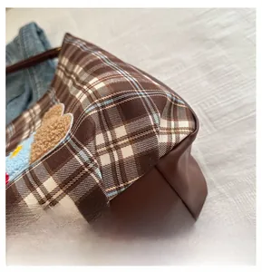 Detail showing the plaid fabric, plush teddy bear patch, and stitching on the tote bag