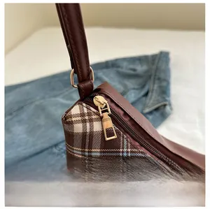 Detail of smooth metal zipper and brown leather strap on plaid crossbody bag