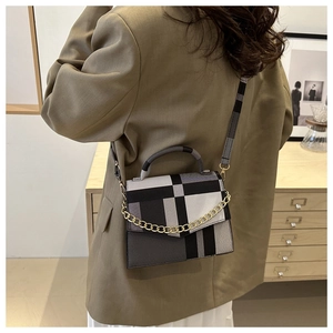 Detail of a geometric checkered crossbody bag featuring a chunky gold chain and wide strap