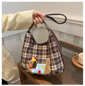 Detail of checkered tote bag with plush puppy patch and brown leather handles