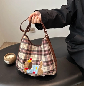 Detail of pink plaid tote bag featuring a cute plush dog patch and brown leather handle