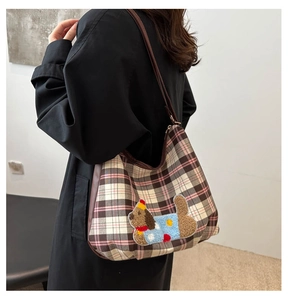 Detail of a pink and brown plaid shoulder bag with a cute plush cartoon puppy patch