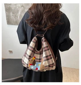 Detail of checkered plaid backpack featuring a plush cartoon dog embroidery and leather trim