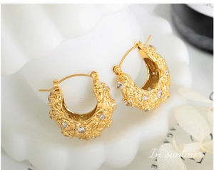 Détail de boucles d'oreilles dorées avec texture de lave et zircon sur coquillage