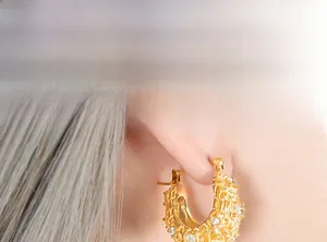 Détail de créoles dorées avec texture gaufrée et pierres de zircone cubiques brillantes