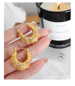 Détail de boucles d'oreilles créoles dorées avec texture irrégulière et zircons cubiques