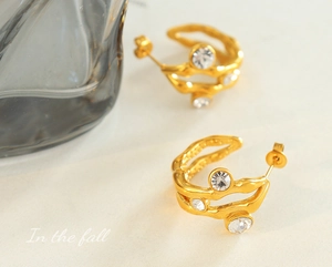 Detail view of gold wave hoop earrings with irregular lava texture and cubic zirconia