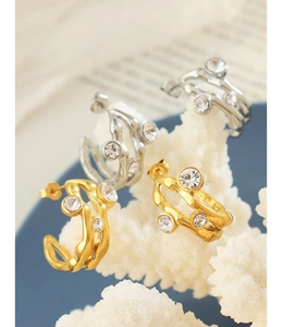 Detail of C-shaped wavy gold and silver earrings with inlaid cubic zirconia