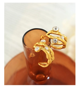 Detail of gold-plated irregular hoops with zircon crystals hanging on a glass rim