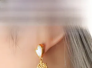 Detailed close-up of gold heart earrings with shell inlay and textured weave drop