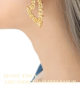 Close-up of golden heart earrings with woven texture worn on ear for size perspective