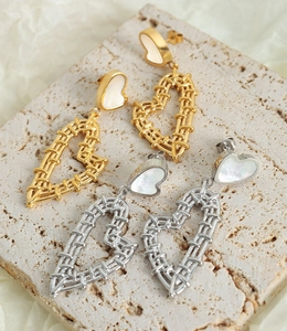 Detail of gold and silver woven heart drop earrings with white shell studs on stone