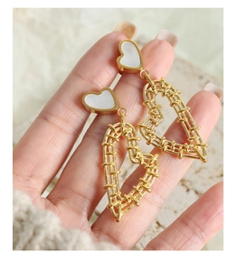 Detail of gold woven heart earrings with white shell inlay held by hand