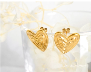Macro shot of gold-plated titanium heart earrings with embossed wavy texture on glass