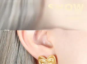 Close-up of model wearing gold heart earrings with unique layered pleated texture