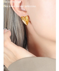 Detail shot of heart-shaped gold stud earrings with elegant wavy texture on model