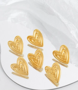Macro shot of gold-plated heart stud earrings with layered concentric textures on white art paper