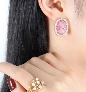 Detail of pink vintage cameo earrings with pearls and layered gold pearl ring on model