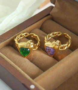Detail of gold braided heart rings with green and purple crystals on brown velvet