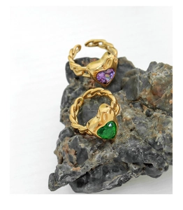 Detail of gold twisted band rings with purple and green heart crystals on rock