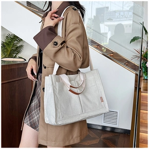 Close-up of white corduroy tote bag featuring brown leather handles and a side fashion label