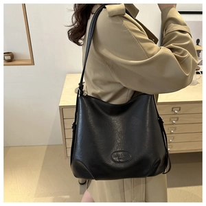 Detail view of black matte PU leather tote bag with embossed logo on model in trench coat