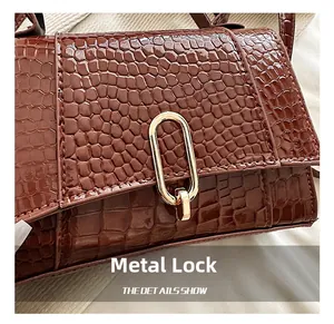 Gros plan sur le cuir crocodile marron et le fermoir ovale en métal doré du sac