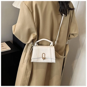 Détail du sac blanc motif crocodile avec boucle dorée porté par un mannequin