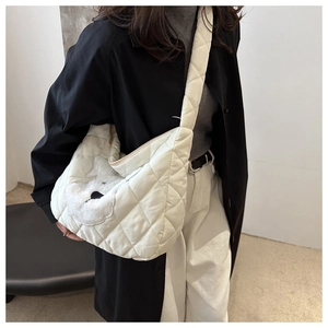 Detail of quilted off-white tote bag featuring a plush animal patch and wide shoulder strap