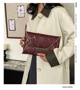 Detail of burgundy textured leather envelope clutch with gold metal trim held by a model