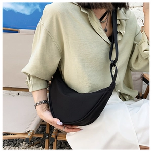 Outdoor lifestyle shot of a black nylon crescent crossbody bag worn by a model in nature