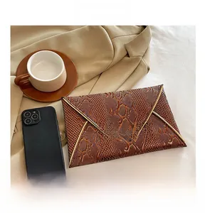 Detail of dark brown faux snake skin clutch bag shown next to a smartphone for size reference