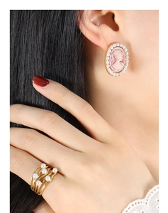 Close-up of elegant pink cameo pearl earrings and layered gold ring on a model