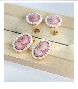 Close-up of pink cameo earrings with white faux pearls and gold metal base