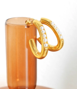 Detailed macro view of gold-plated C-shaped earrings with pearls on a glass rim