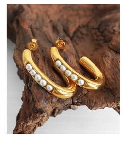 Detail of gold U-shaped titanium steel earrings inlaid with five white pearls on wood