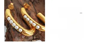 Macro detail of U-shaped gold earrings featuring minimalist pearl inlay on a dark wood base