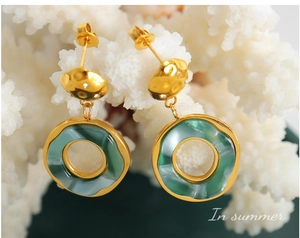 Close-up of 18K gold plated hoop earrings with green resin rings on white coral