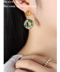 Detailed shot of gold earrings with green resin rings and a wave pearl ring on a model