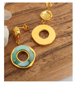Detail of 18K gold earrings with green resin stone and sparkling rhinestones on wood