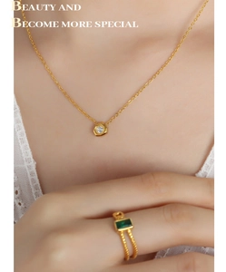 Close-up of a gold necklace with round zircon and double-layer green gemstone ring
